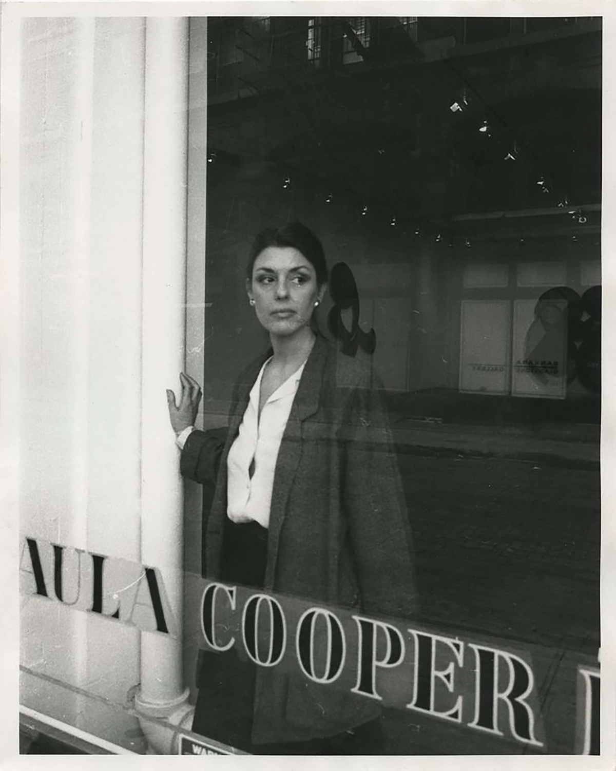 Black and white photo of Paula Cooper in the window of her gallery