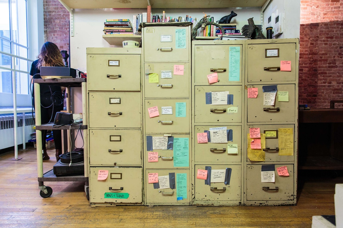 A color photograph of tan filing cabinets covered in pink, orange, and turquoise post-it notes in the studio of Mary Beth Edelson.